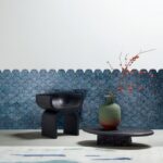 Moderne interieursetting met Arte Camber 33732 behang in blauw visgratenpatroon, een zwarte designstoel en een lage tafel met vaas en rode takken.