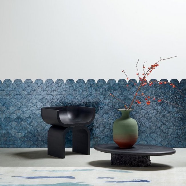 Moderne interieursetting met Arte Camber 33732 behang in blauw visgratenpatroon, een zwarte designstoel en een lage tafel met vaas en rode takken.