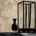 Zwarte vaas en houten sculpturen in vitrine voor Arte behang Capas 34307 met natuurlijke textuur.