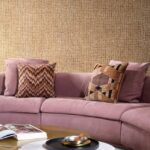 Roze fluwelen bank met sierkussens voor een muur met Arte Cashmere 73061 behang in een warme textuur.