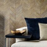 Luxe interieur met Arte behang Corteza 34202 in visgraatpatroon, een crèmekleurige fauteuil en donkere kussens.