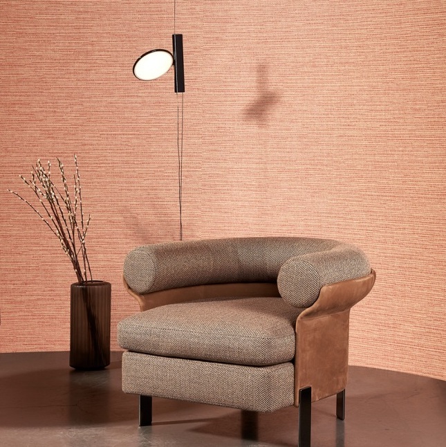 Bruin Arte Koumbala behang met een ronde fauteuil, moderne wandlamp en vaas met takken in een minimalistisch interieur.