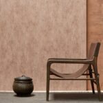 Luxe interieur met Arte behang Manchas in warme aardetinten, houten loungestoel en decoratieve mand.