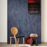 Moderne interieursetting met Arte Manchas behang in blauw, een houten designstoel, een zwarte bijzettafel met boeken en een rood decoratief object.
