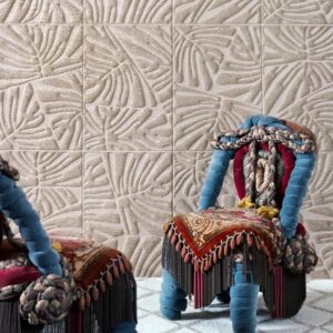 Twee opvallende stoelen met kleurrijke bekleding staan voor een wand met Arte Monstera behang met een reliëf van tropische bladeren.