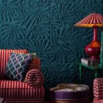 Interieur met donkerblauw Arte Monstera 43022 behang, rood-wit gestreeelde bank en kleurrijke accessoires.