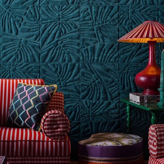 Interieur met donkerblauw Arte Monstera 43022 behang, rood-wit gestreeelde bank en kleurrijke accessoires.
