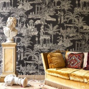 Interieur met zwart Arte-behang in mythologisch Grieks thema, een klassieke buste op sokkel en een fluwelen gele bank.