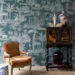 Wand met Arte-behang in Griekse mythologische stijl, gecombineerd met een klassieke fauteuil en oosters kabinet.