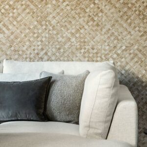Lichtbeige bank met sierkussens voor een wand bekleed met Arte behang Pandan 34104 in gevlochten patroon.