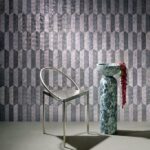 Moderne interieursetting met Arte behang Prisma 33710, een metalen stoel en een marmeren sokkel met schaal en bloemen.