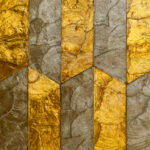 Geometrisch Arte-behang Prisma 33712 met een patroon van goud- en bronskleurige texturen in visgraatmotief.