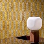 Moderne ruimte met Arte Prisma 33712 behang in goud- en grijstinten en een designlamp met houten voet en witte bolvormige kap.