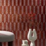 Stijlvolle interieurhoek met Arte behang Prisma 33713 in roodtinten, moderne vazen en een grijze poef.