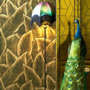 Sfeervolle interieurhoek met Arte behang Bird of Paradise, een kleurrijke lamp en een decoratieve pauw.