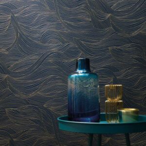 Donkerblauw CASAMANCE Alula-behang met goudkleurig golvend patroon, met decoratieve objecten op een groen bijzettafeltje.
