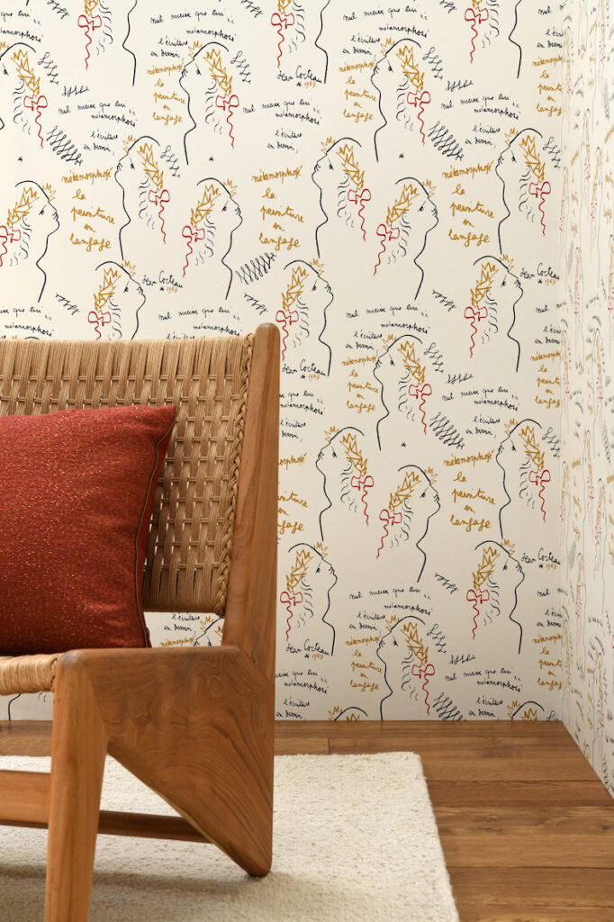Houten stoel met rood kussen staat voor een muur met artistiek ECRITURE-behang met getekende profielen en handgeschreven teksten.