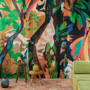 Kleurrijk Elitis Begur VP 927 01 behang met abstract tropisch motief in een sfeervol interieur met rotan elementen en een groene bank.