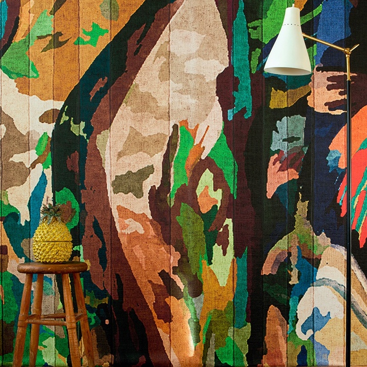 Kleurrijk Elitis Begur VP 927 01 behang met abstract patroon, houten krukje met ananas en witte wandlamp.