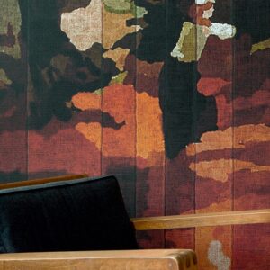 Detail van het Elitis Cordoba VP 926 01 behang met abstract bloemmotief in warme tinten achter een houten stoel met zwarte bekleding.