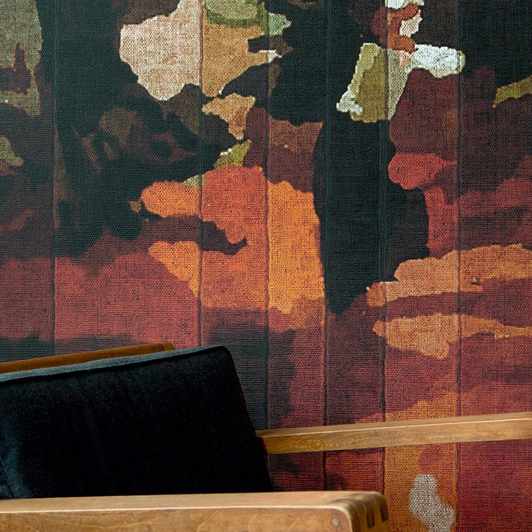 Detail van het Elitis Cordoba VP 926 01 behang met abstract bloemmotief in warme tinten achter een houten stoel met zwarte bekleding.