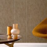 Bruin Elitis Corinthe behang met een oranje designstoel en matte vazen op een houten tafel.