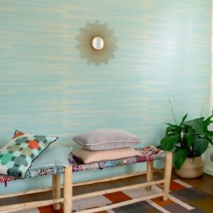 Interieur met Elitis behang Kari VP 930 40 in turquoise tint, een houten bank met kussens, een groene plant en een decoratieve spiegel aan de muur.