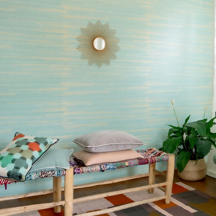 Interieur met Elitis behang Kari VP 930 40 in turquoise tint, een houten bank met kussens, een groene plant en een decoratieve spiegel aan de muur.