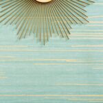 Detail van Elitis behang Kari VP 930 40 met turquoise achtergrond en goudkleurige horizontale accenten, gecombineerd met een decoratieve zonnespiegel.