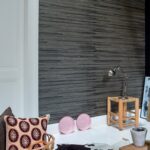 Moderne interieurhoek met Elitis behang Kari VP 930 80, houten krukje, industriële lamp en decoratieve accessoires.