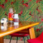 Houten tafel met vintage vazen en kleurrijk Elitis La Californie behang met vogels en palmblaadjes op de achtergrond.