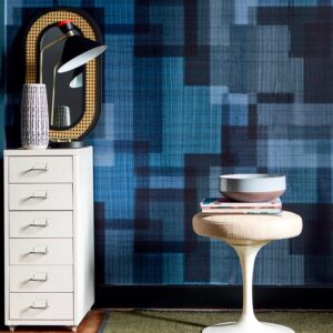 Interieur met Elitis Madras VP 931 80 behang in blauwtonen, een witte ladekast, spiegel met lamp en een designkruk met boeken en een schaal.