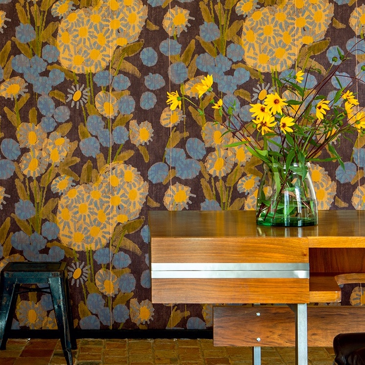 Vrolijk bloemenbehang uit de Elitis Margaritas collectie met gele en blauwe bloemen tegen een donkere achtergrond.