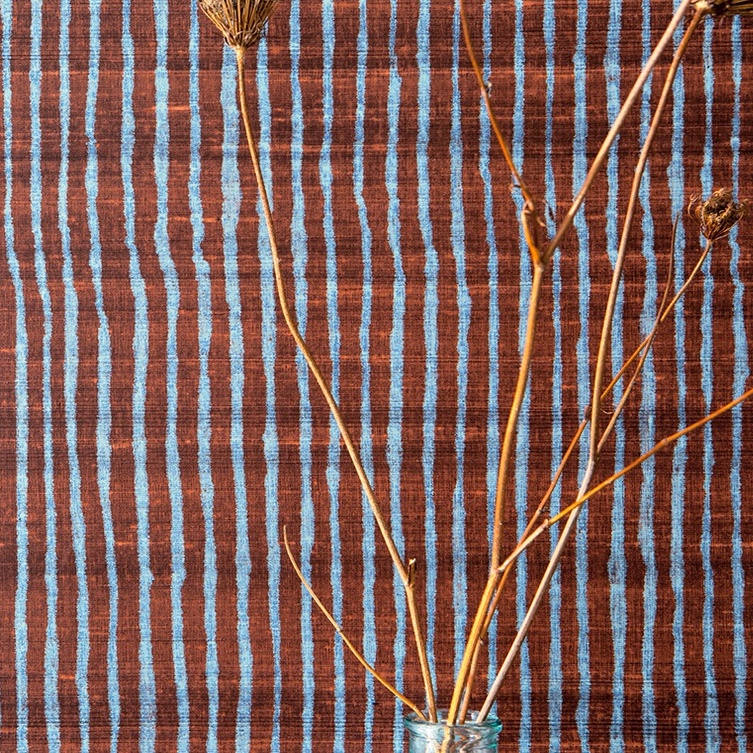 Gedroogde takken in een glazen vaas voor een Elitis Nila VP 929 50 behang met blauwbruine verticale strepen.