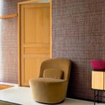 Moderne interieurhoek met Elitis Nila VP 929 50 behang, een fluwelen fauteuil en houten deur.