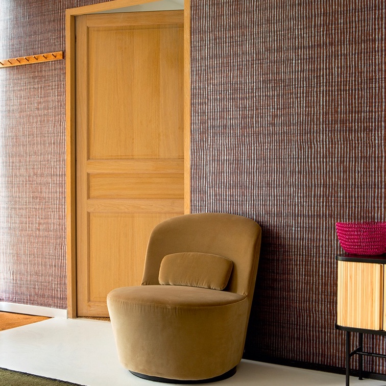 Moderne interieurhoek met Elitis Nila VP 929 50 behang, een fluwelen fauteuil en houten deur.