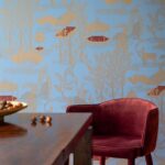 Velvet rode stoel en houten tafel voor een blauw Elitis Siam TP 320 03 behang met goudkleurige oosterse motieven.