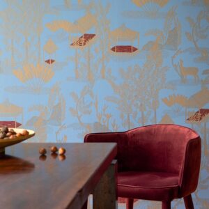 Velvet rode stoel en houten tafel voor een blauw Elitis Siam TP 320 03 behang met goudkleurige oosterse motieven.