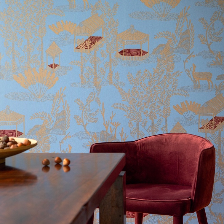 Velvet rode stoel en houten tafel voor een blauw Elitis Siam TP 320 03 behang met goudkleurige oosterse motieven.