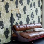Leren chaise longue voor een wand met Elitis Ulysse VP 925 01 behang met zwarte vazen en plantenmotief.