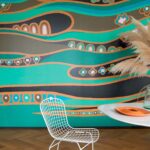Kleurrijk Elitis Una Storia TP 326 01 behang met golvende patronen in turquoise, oranje en zwart, gecombineerd met een modern interieur.