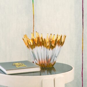 Decoratieve glazen schaal met goudaccenten op een ronde tafel voor Elitis Volos behang met kleurrijke verticale lijnen.