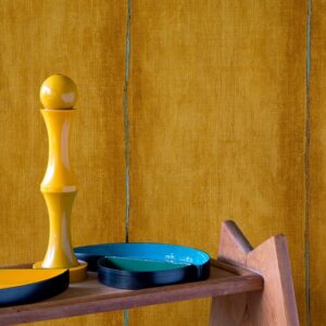 Gele wand met Elitis Volos behang VP 921 05, met kleurrijke decoratie op een houten plank.
