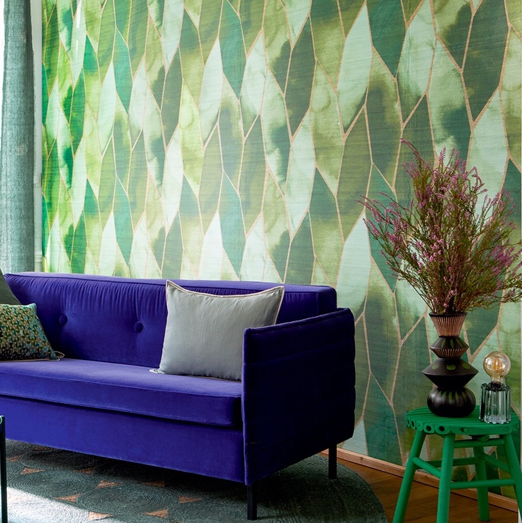 Een interieur met Elitis Yuzen VP 932 60 behang in groene tinten, een paarse fluwelen bank en een groene bijzettafel met een vaas bloemen.