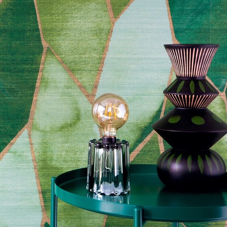 Groen Elitis behang uit de Yuzen collectie met een geometrisch patroon, gecombineerd met een glazen tafellamp en decoratieve zwarte vazen.