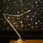 Moderne bureaulamp voor een zwart behang met gouden en koperkleurige illustraties uit de collectie Behangstudio JOYAUX.