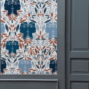 Decoratief Lelievre behang (model CAP D'AIL 6470-03) met symmetrisch patroon van bladeren en gestileerde gezichten in blauw, roodbruin en wit.