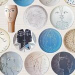 Behang met illustratieve Cocteau-stijl dessins van gezichten en abstracte vormen op kleurrijke ronde keramiekvormen.
