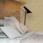 Slaapkamer met Missoni Tweed behang, houten hoofdbord, sierkussens en een zwarte leeslamp.