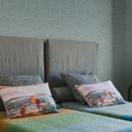 Sfeervolle slaapkamer met Missoni behang uit de Tweed-collectie en kleurrijke sierkussens op een bed met grijze hoofdborden.